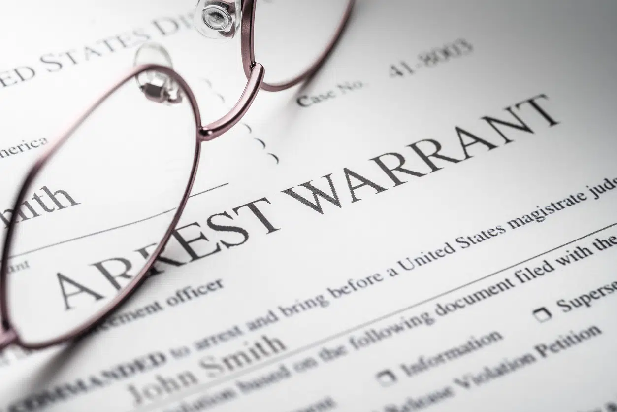 Close up of an "Arrest Warrant" document partially covered by reading glasses.