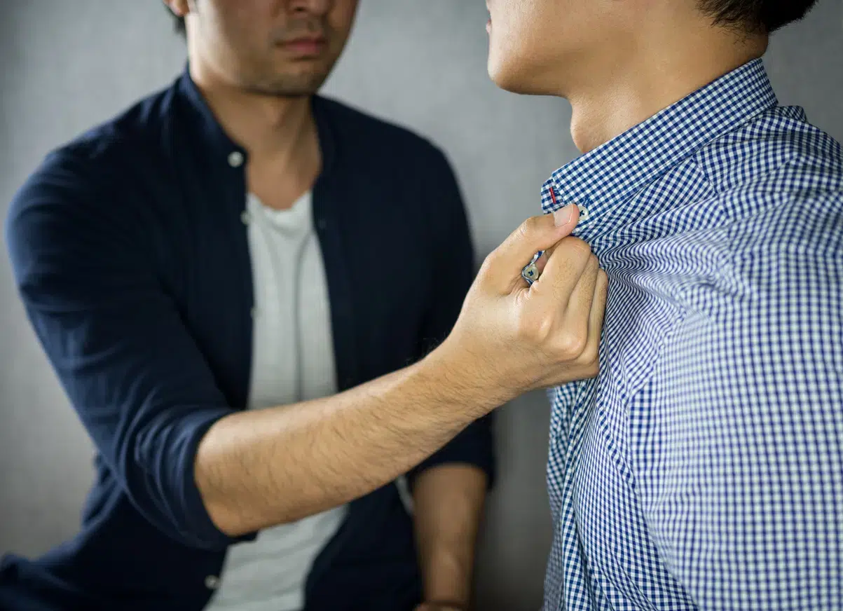 A man in a dark shirt assaults a man in  blue checkered collar.