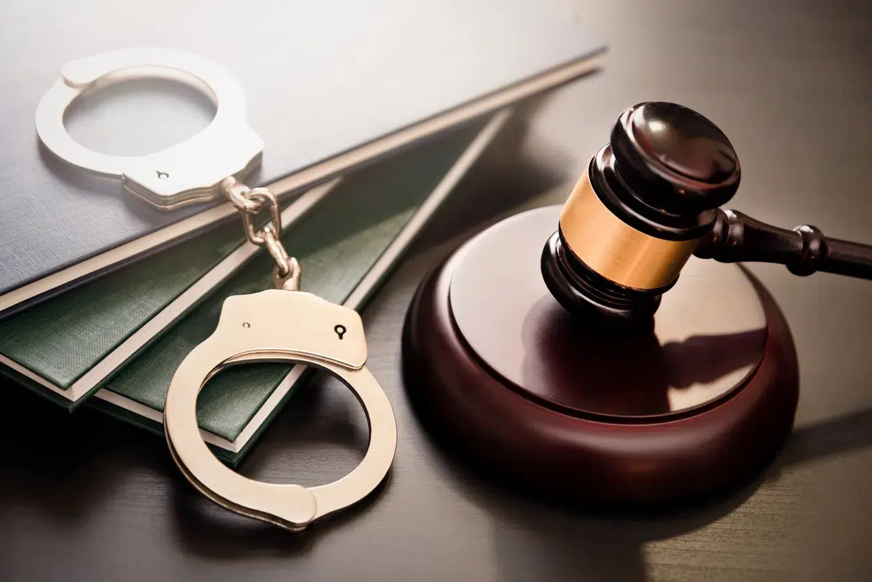 A judge's gavel rests on a wooden block beside silver handcuffs and legal books