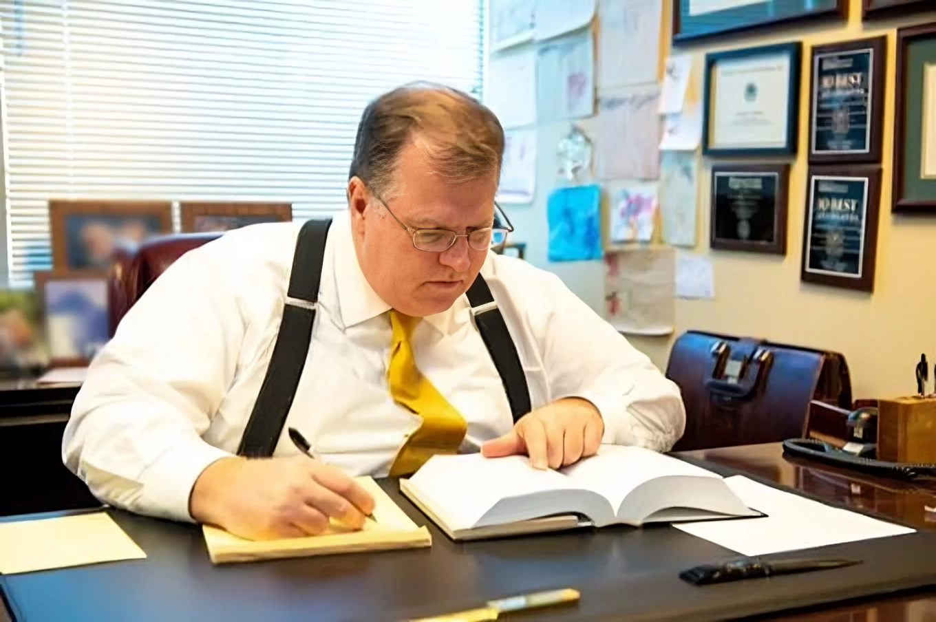 Attorney Scott C. Nolan writes in a notebook while reading a large book at a desk.
