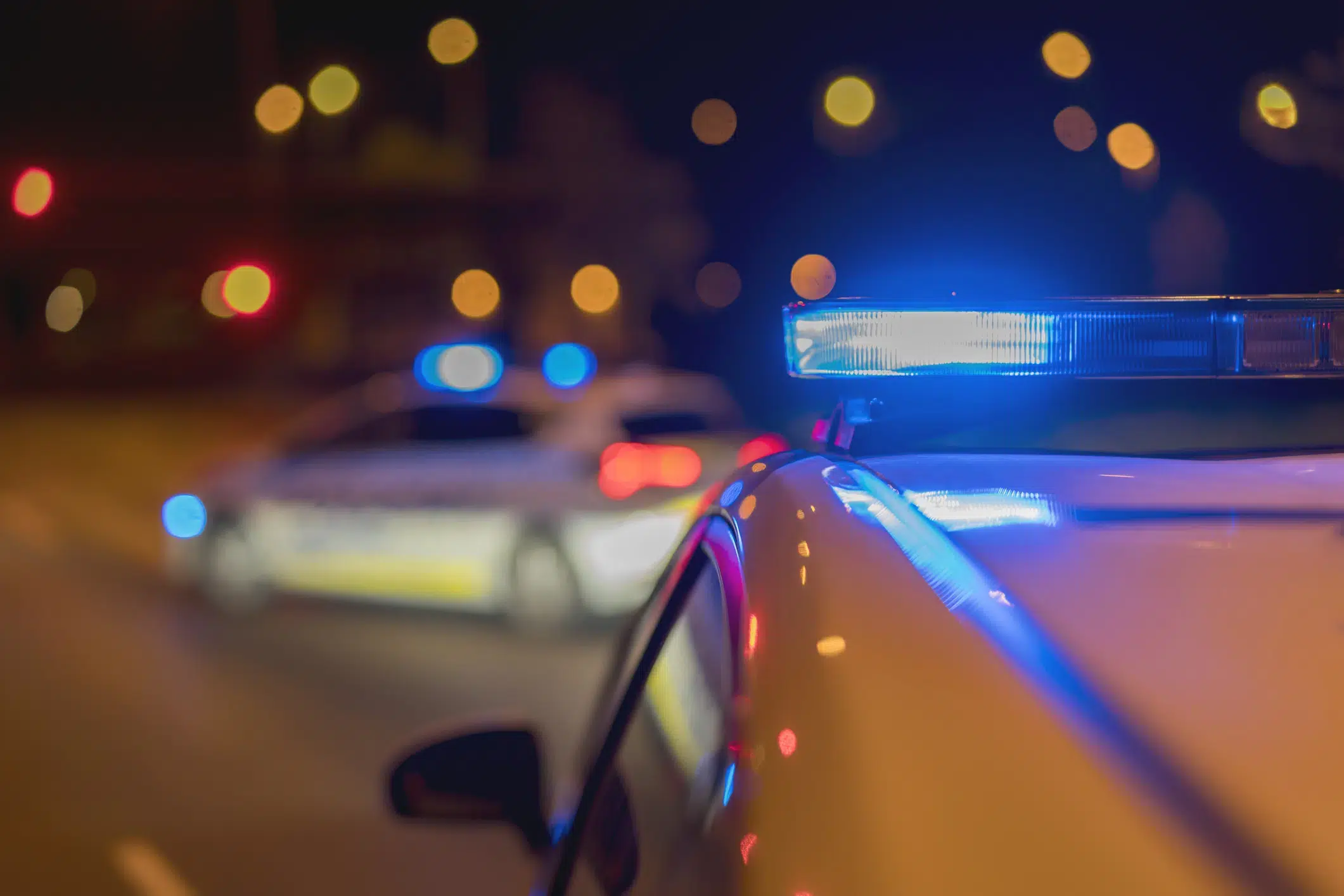 Police cars with flashing blue lights at night, blurred streetlights in the background.